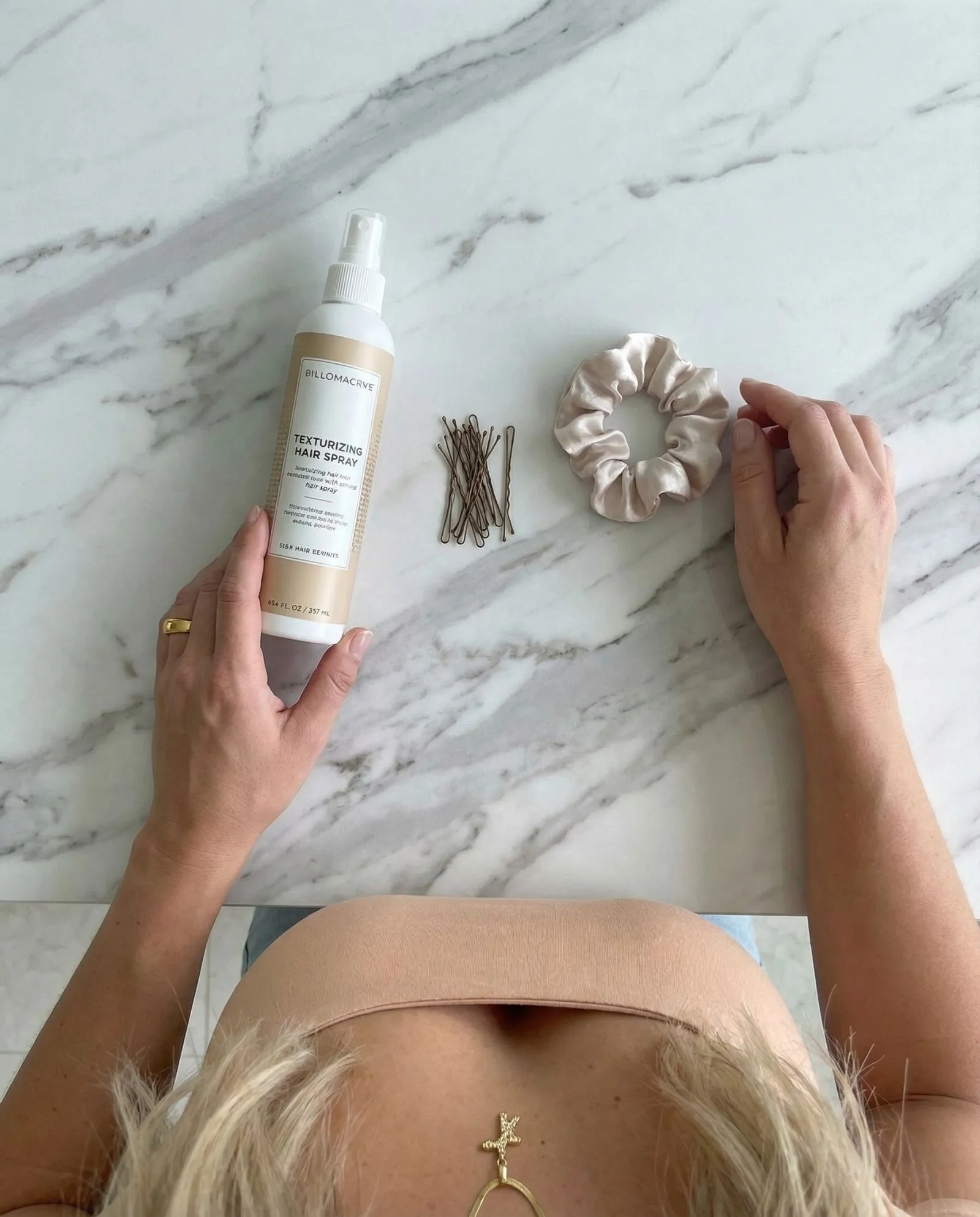 Flat lay of texturizing spray, bobby pins, and silk scrunchie on marble