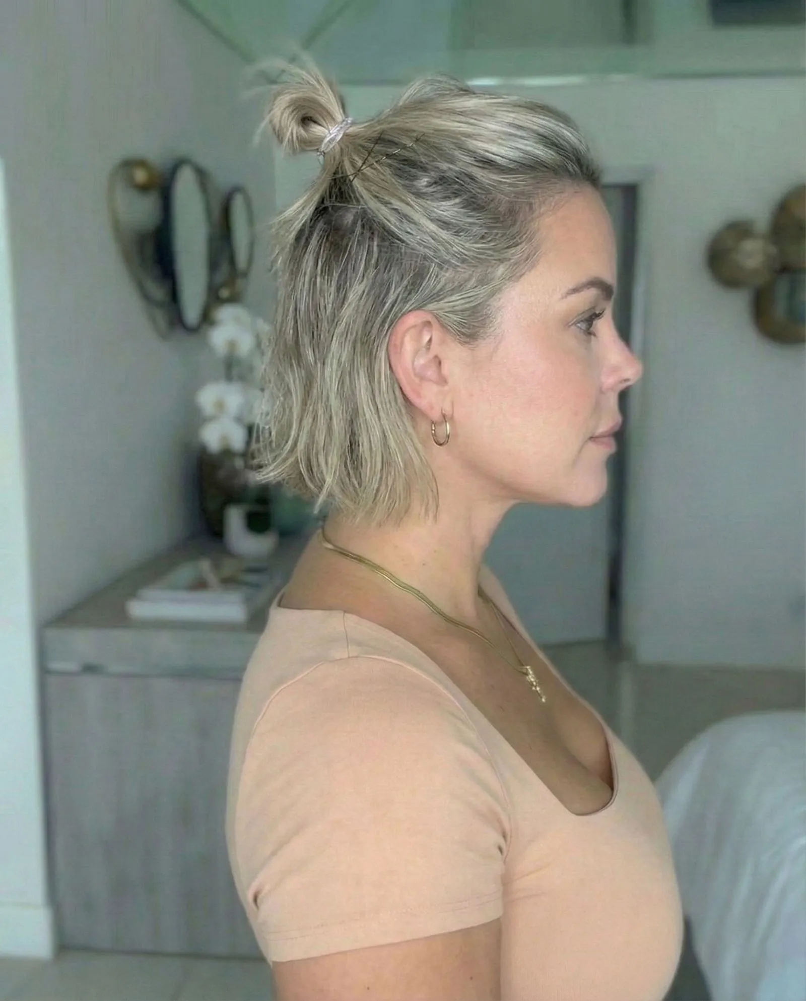 Side profile of a woman styling a half-up top knot with shoulder-length textured hair