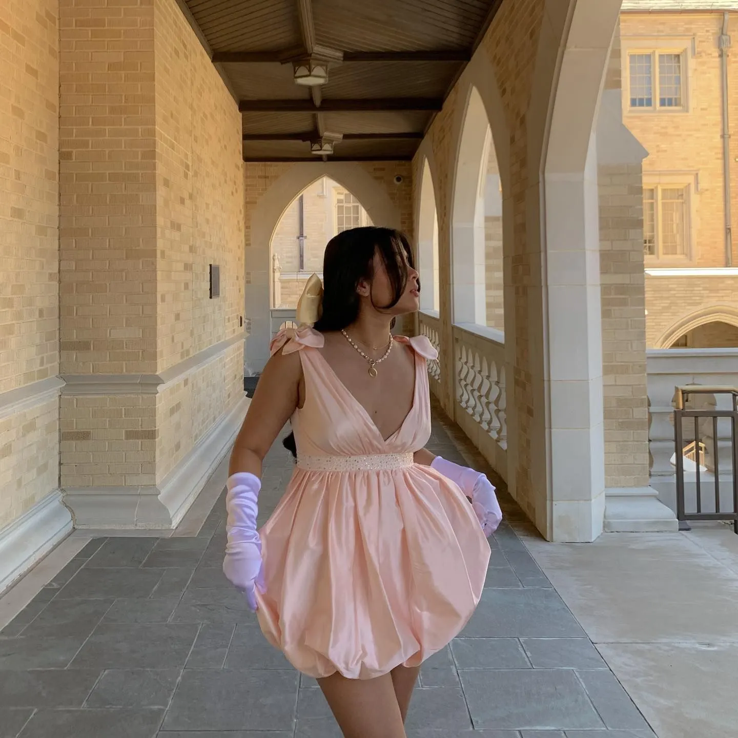 Woman wearing a champagne satin mini dress with dainty pink bows and ruffled hemline for Valentine