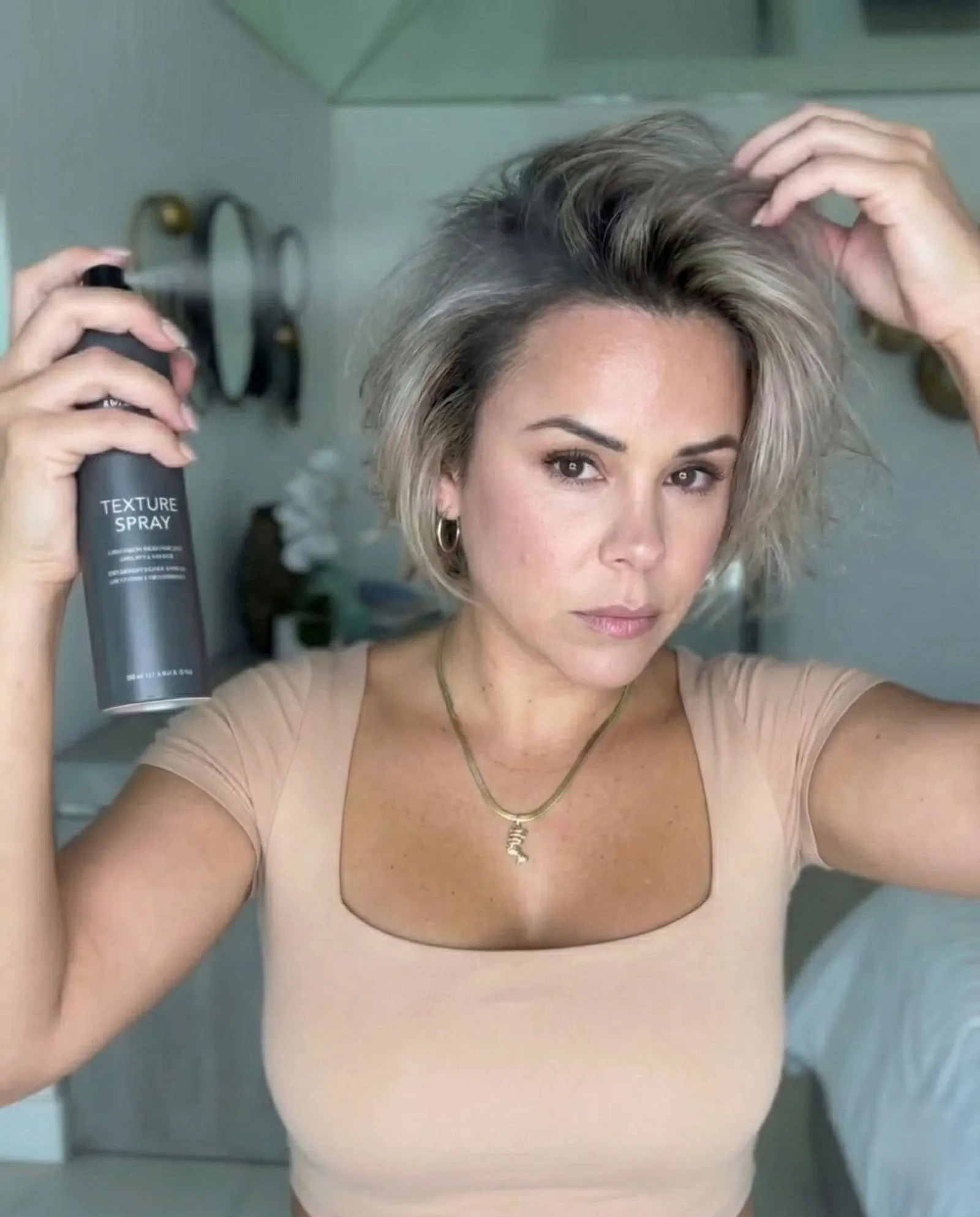 Model tousling grown-out bob hairstyle with texturizing spray for volume