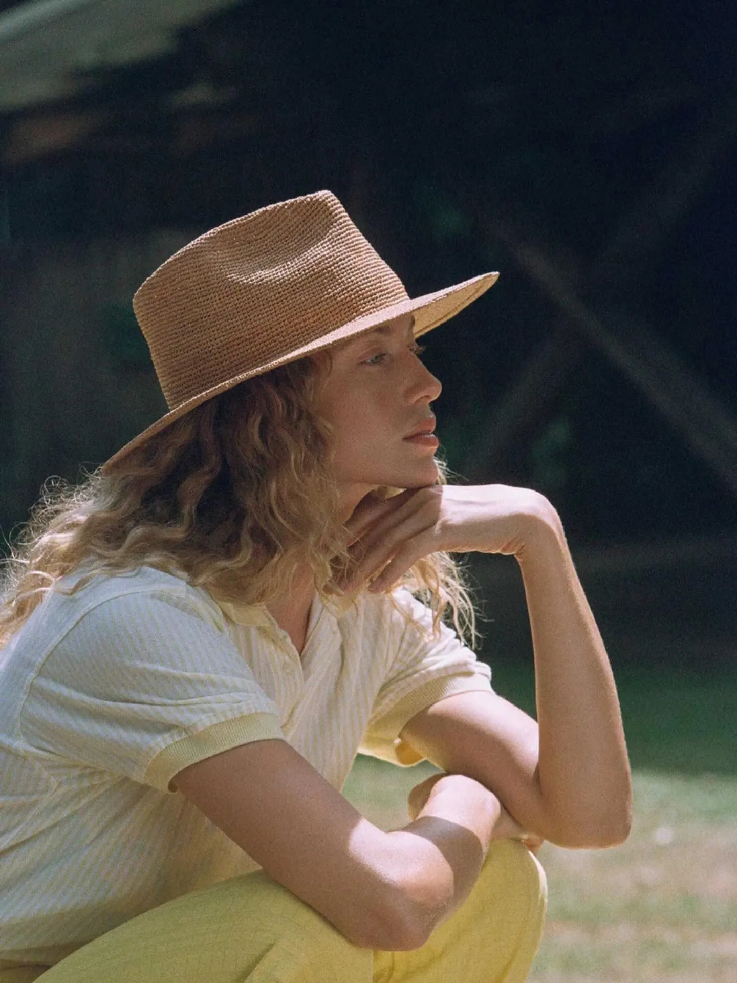 Model wearing an oversized wide-brim raffia hat with dramatic shadows