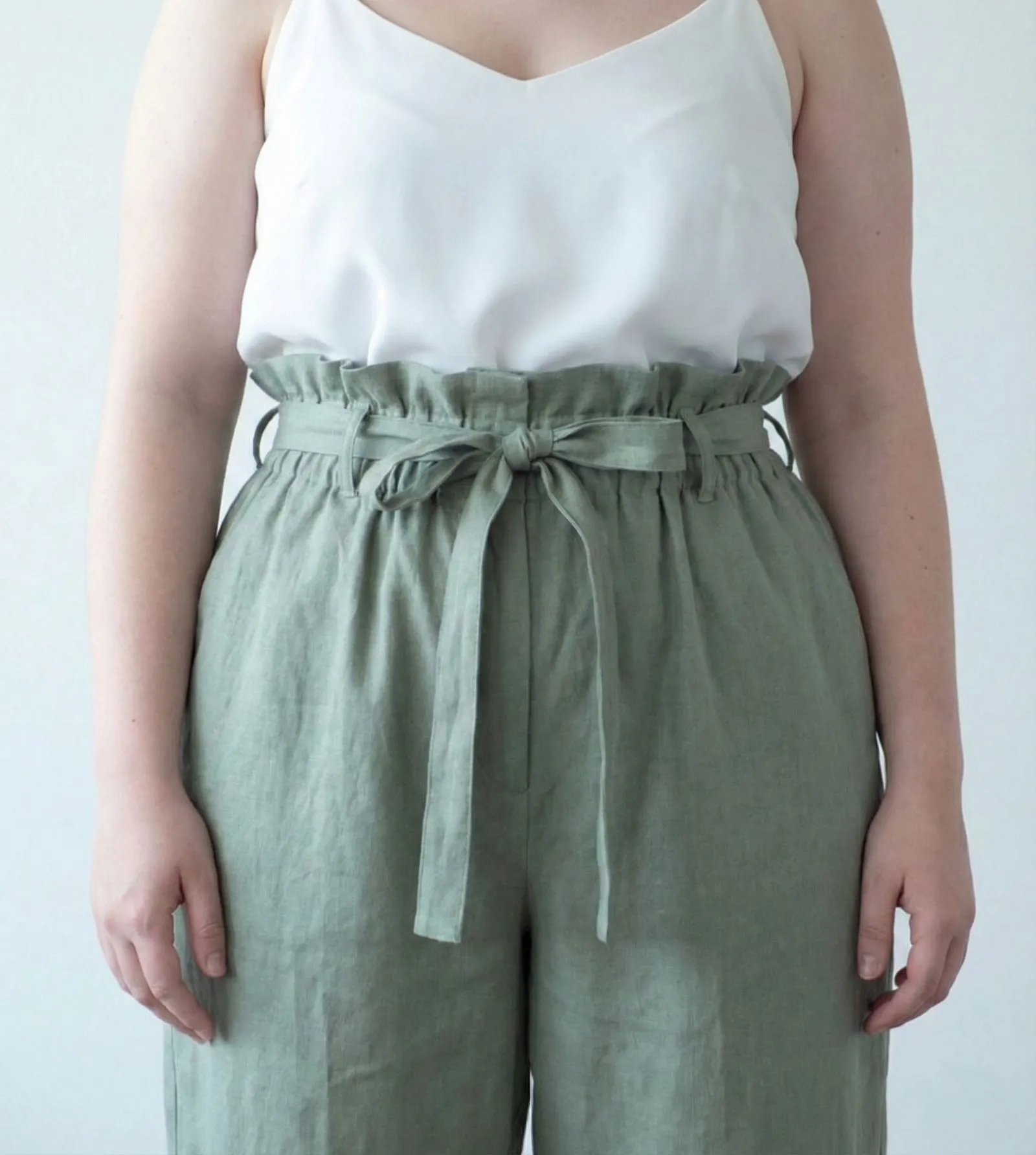 Detail of cinched paperbag waist on sage green wide-leg trousers