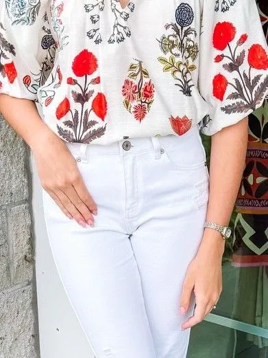 Close up of floral silk blouse tucked into white jeans with gold accessories