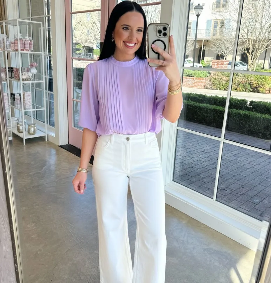 Woman wearing high-waisted white denim trousers and a lavender chiffon blouse in a garden setting