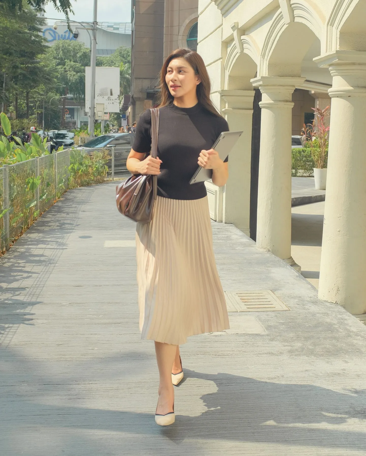 Woman in sand-colored pleated skirt and loafers on a park bench