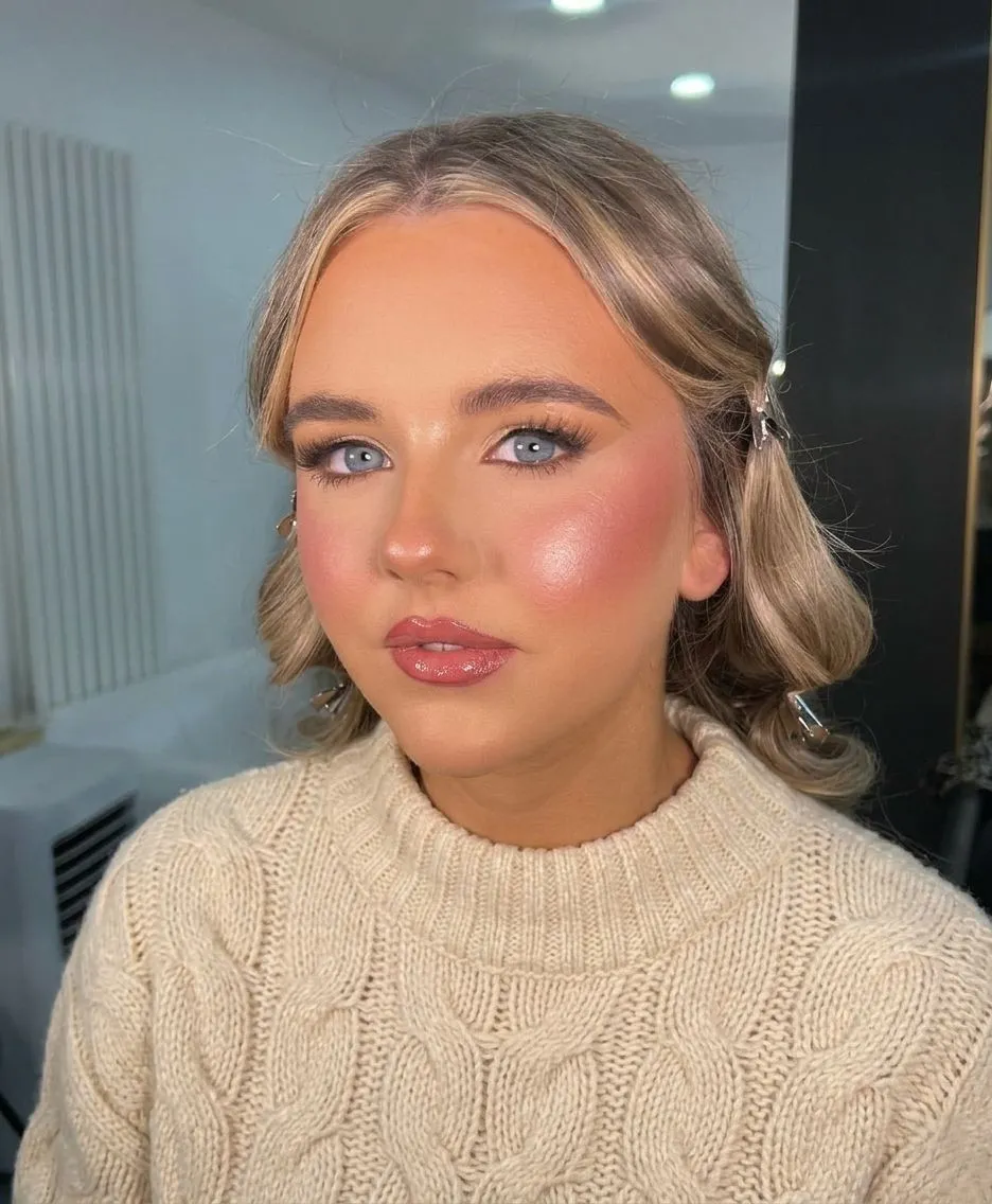 Woman with glowing dewy makeup and sheer berry blush wearing a cozy knit sweater