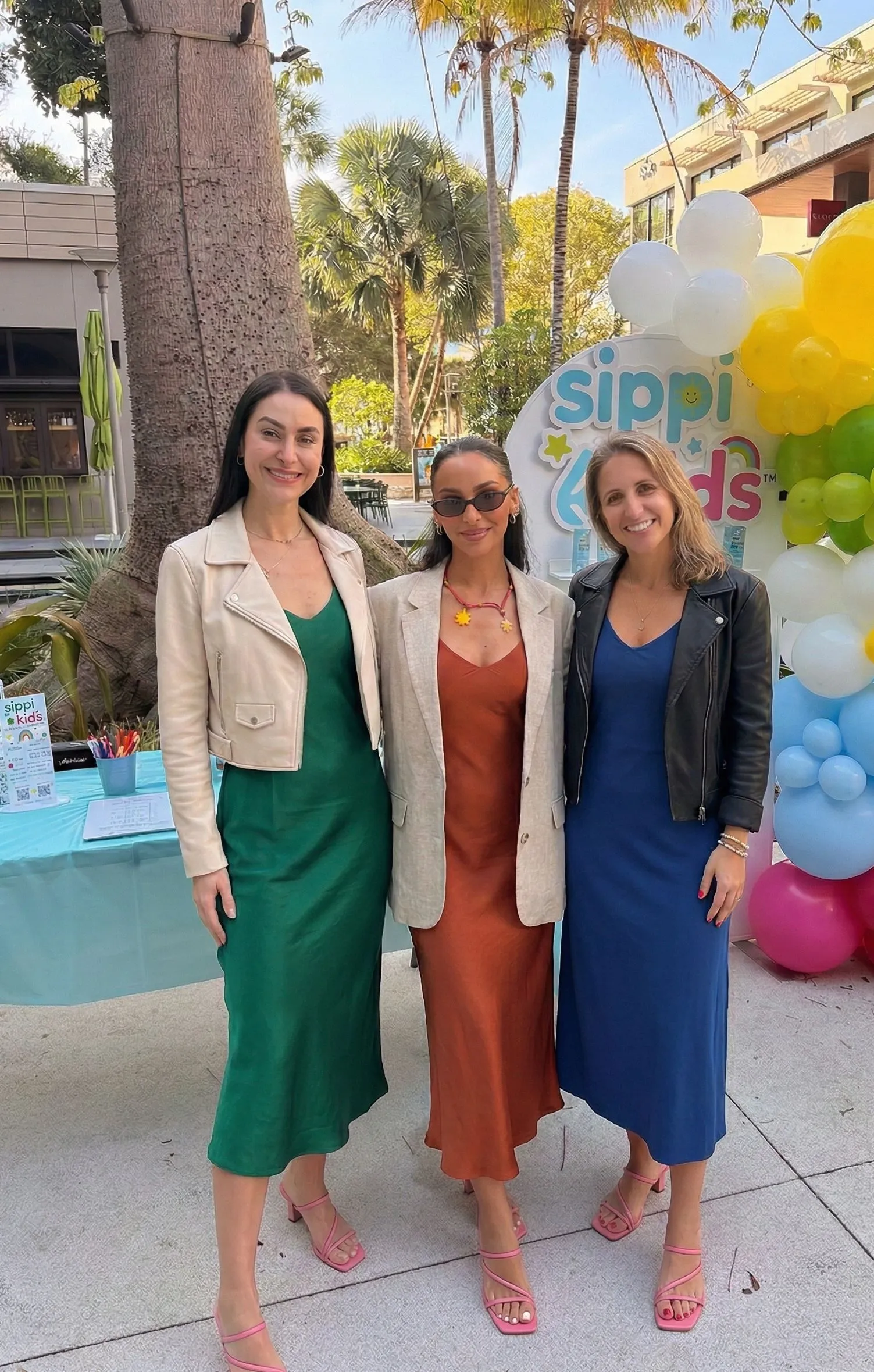 Three stylish women wearing different colored slip dresses and jackets at night
