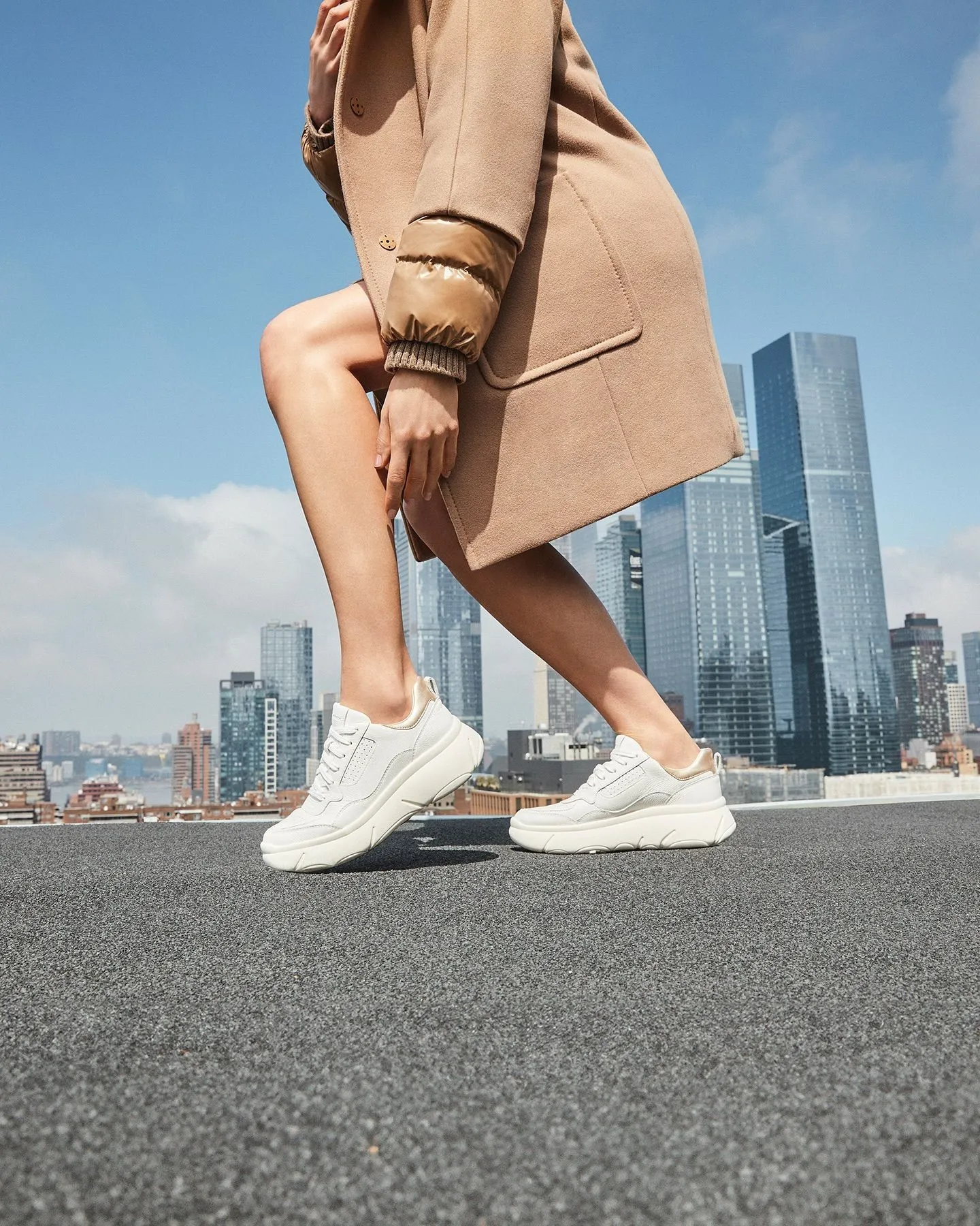 Woman wearing a monochromatic camel outfit with cream platform sneakers on a cobblestone street