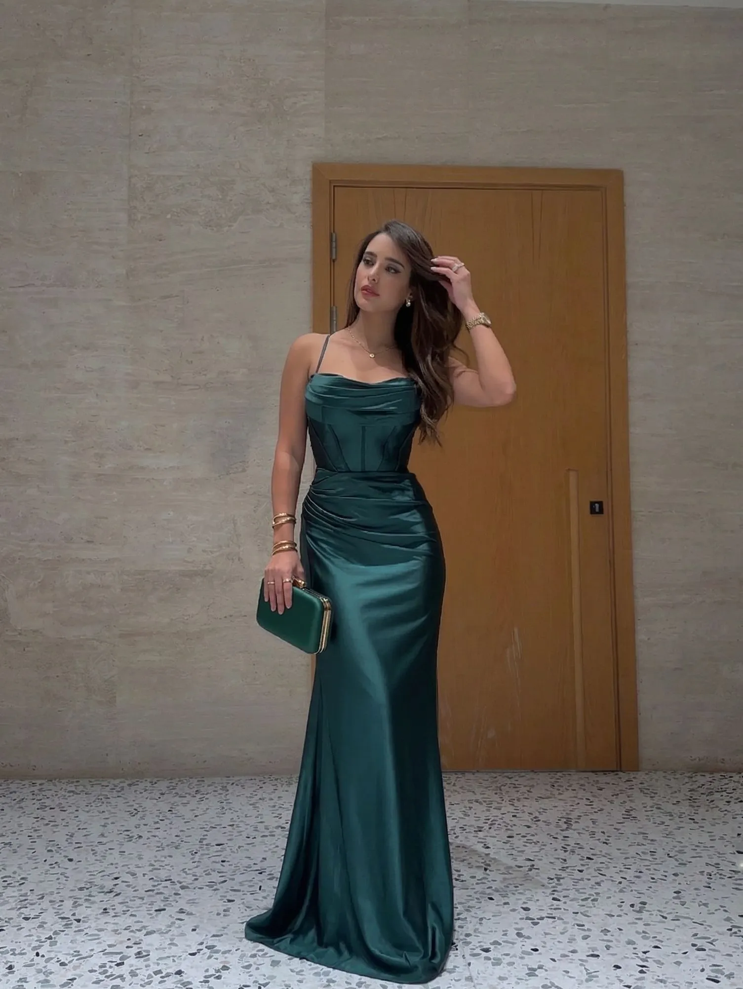 Gold jewelry and silk clutch held by a woman in a formal dress.