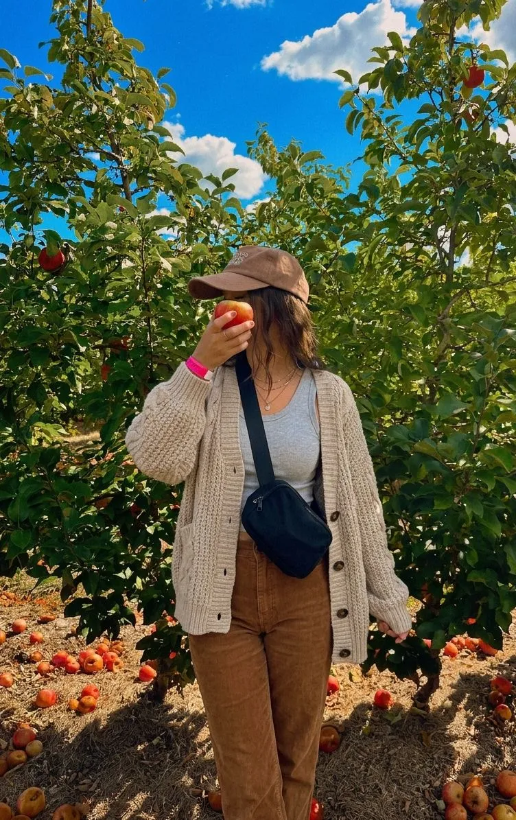 Woman wearing an oversized knit cardigan with vintage wash corduroy trousers in an orchard