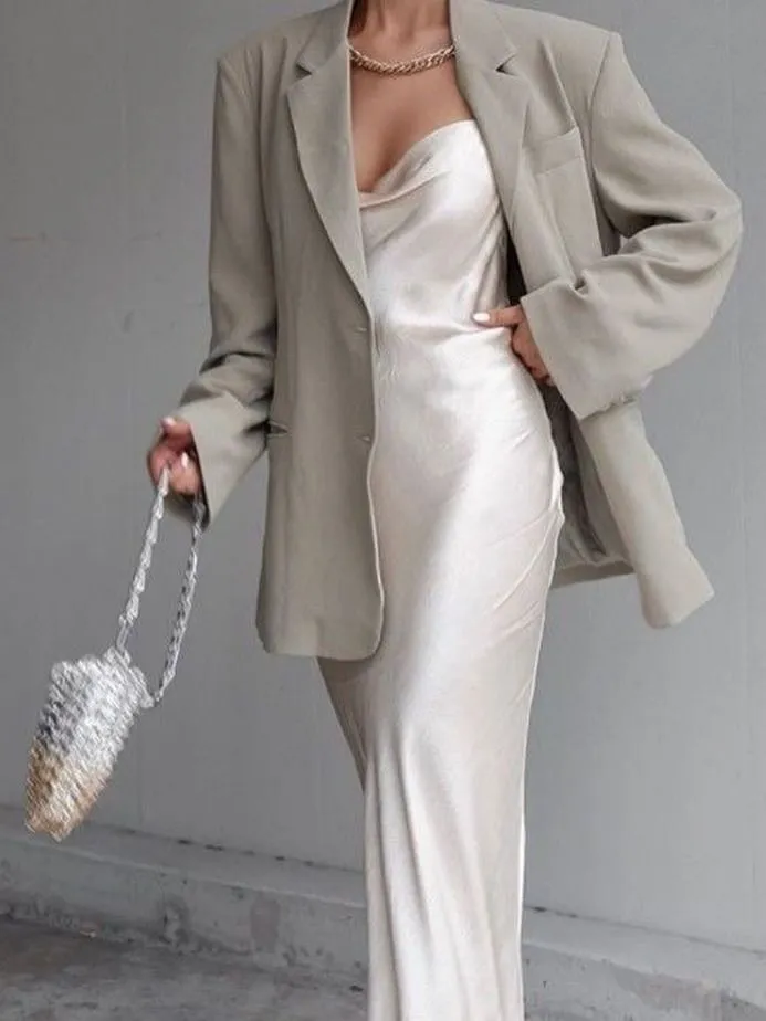 A woman styling a champagne silk dress with a white linen blazer for a summer evening