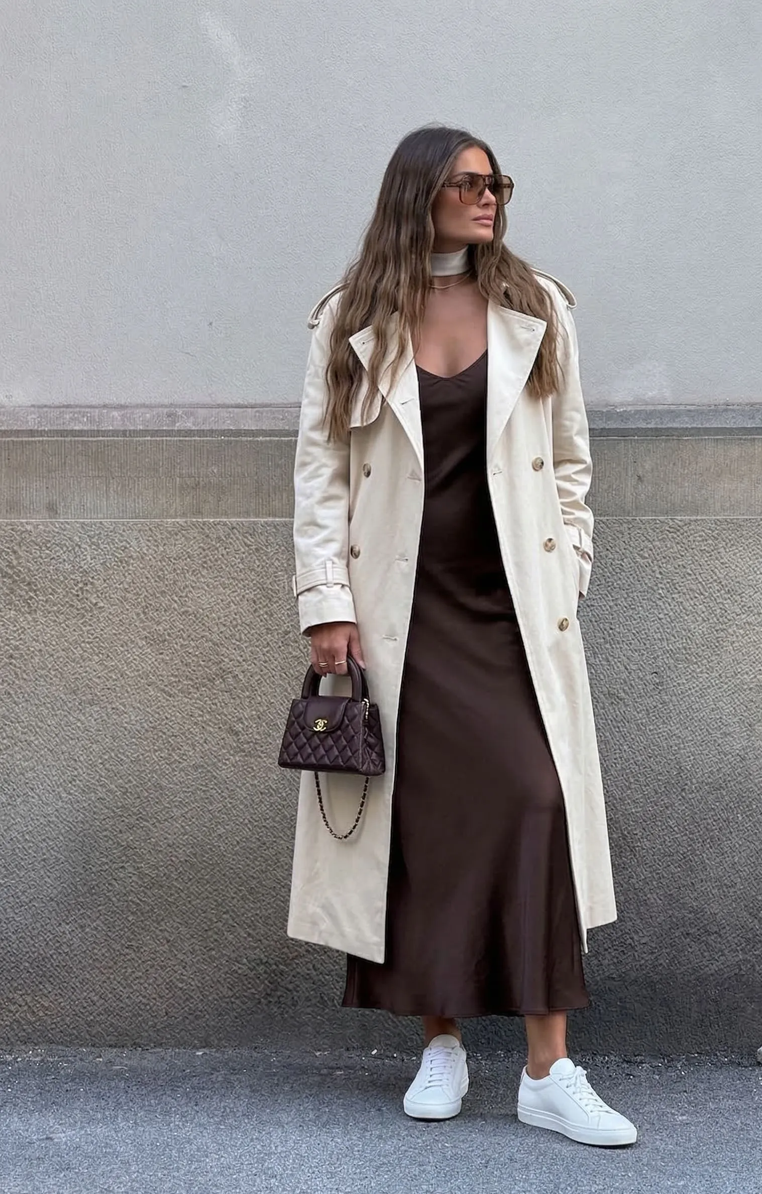 Espresso silk slip dress worn under a cream trench coat with white sneakers