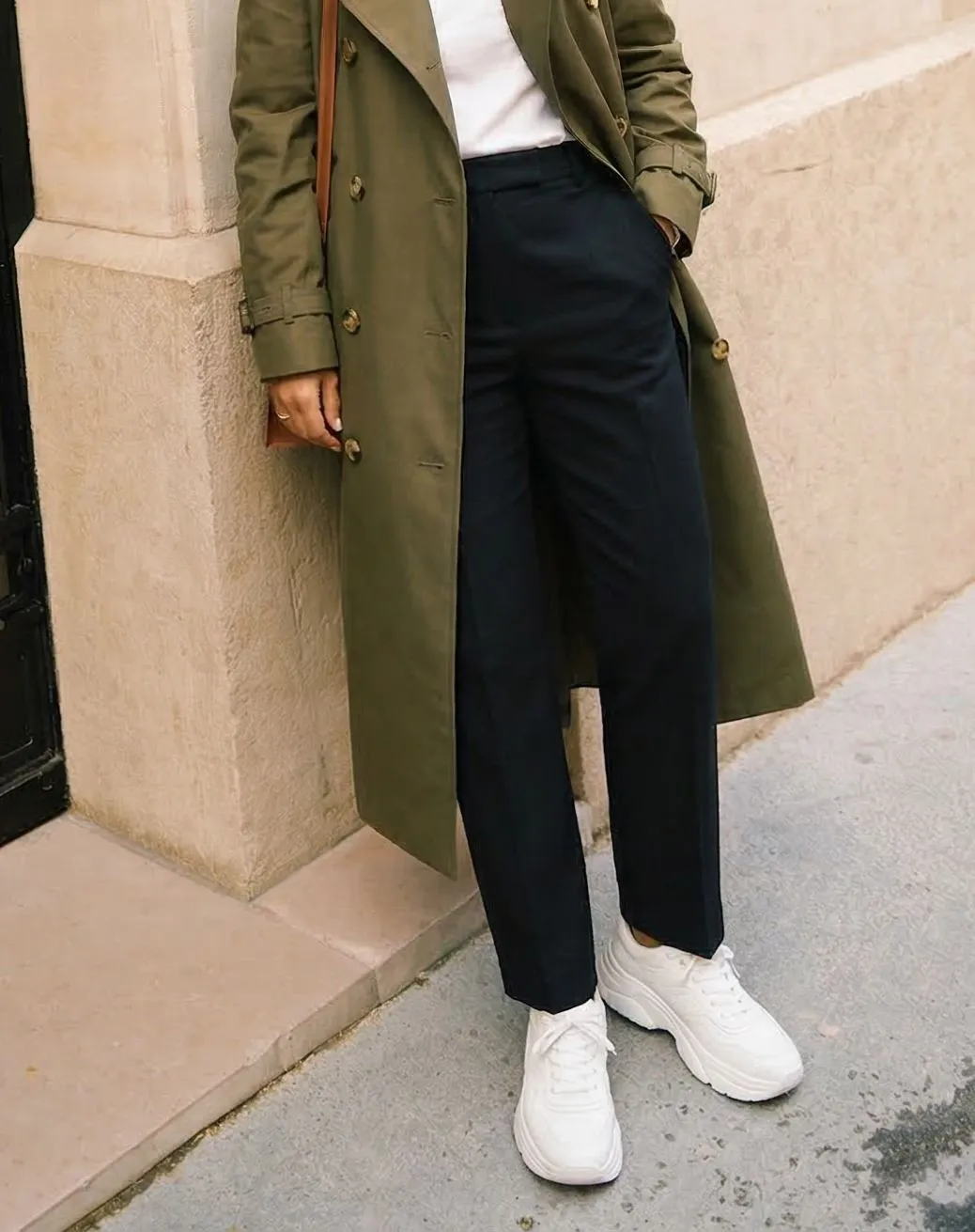 White leather court shoes worn with olive trench coat and tailored trousers