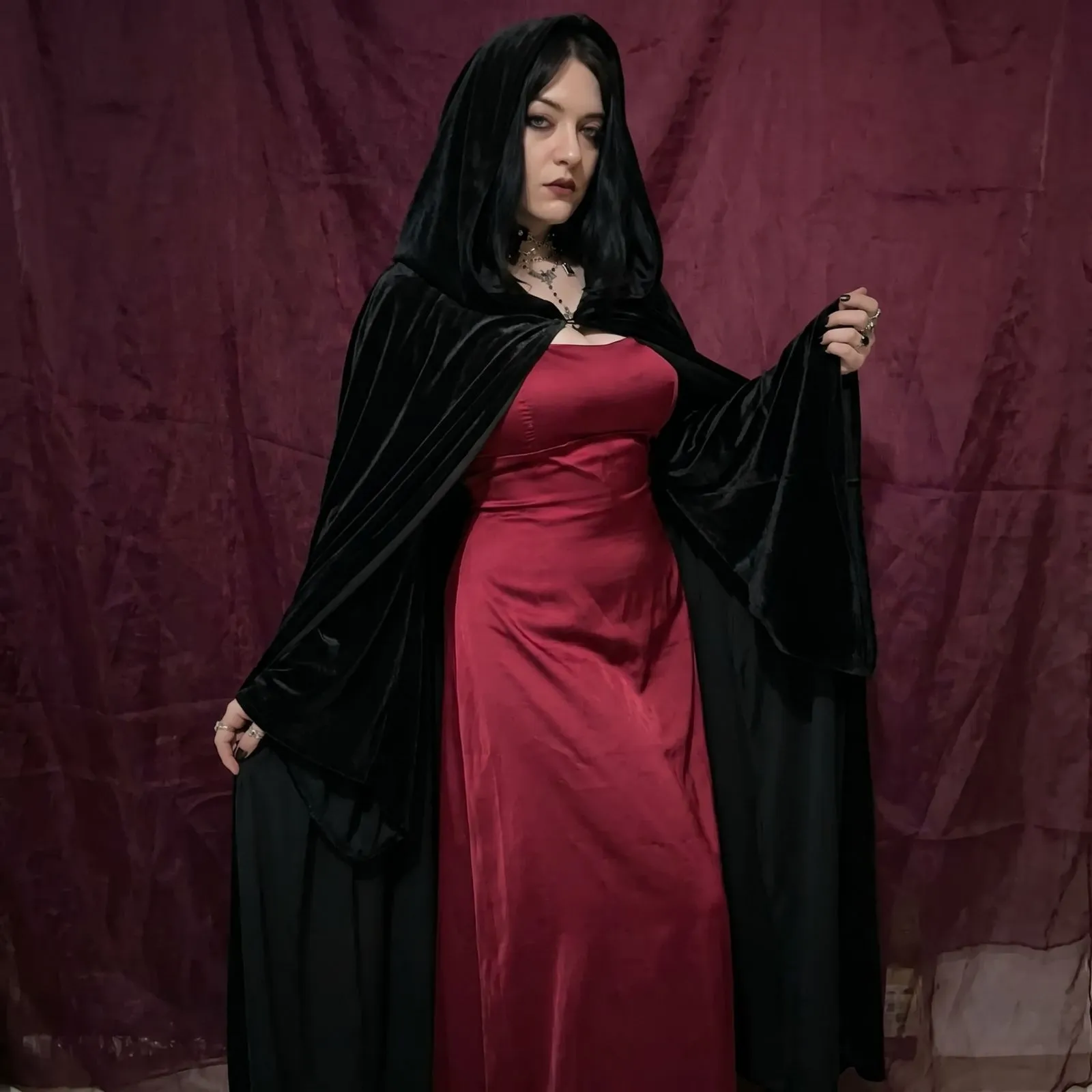 Plus size woman wearing a dramatic floor-length black velvet cape and crimson silk dress for a gothic masquerade