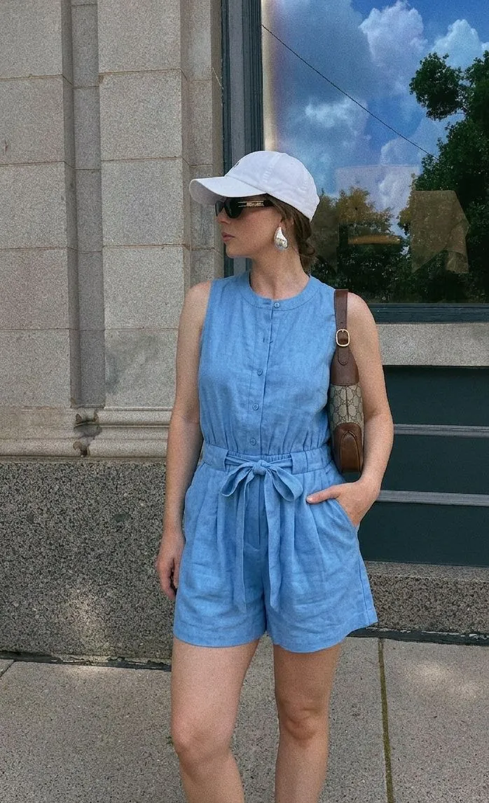 A woman in a sky blue romper and white baseball cap at a baseball game