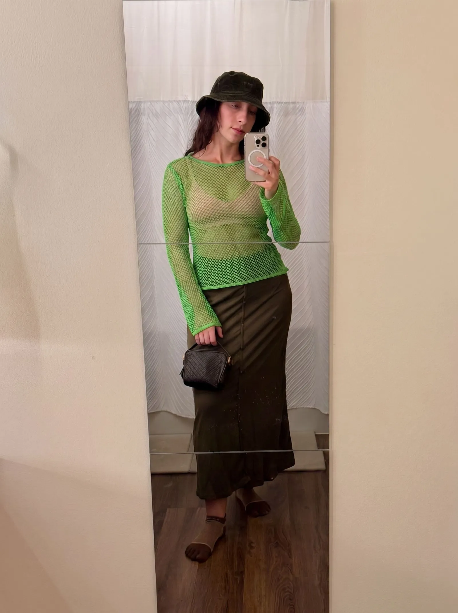 Model with dark skin wearing a bright green mesh top and nude bralette