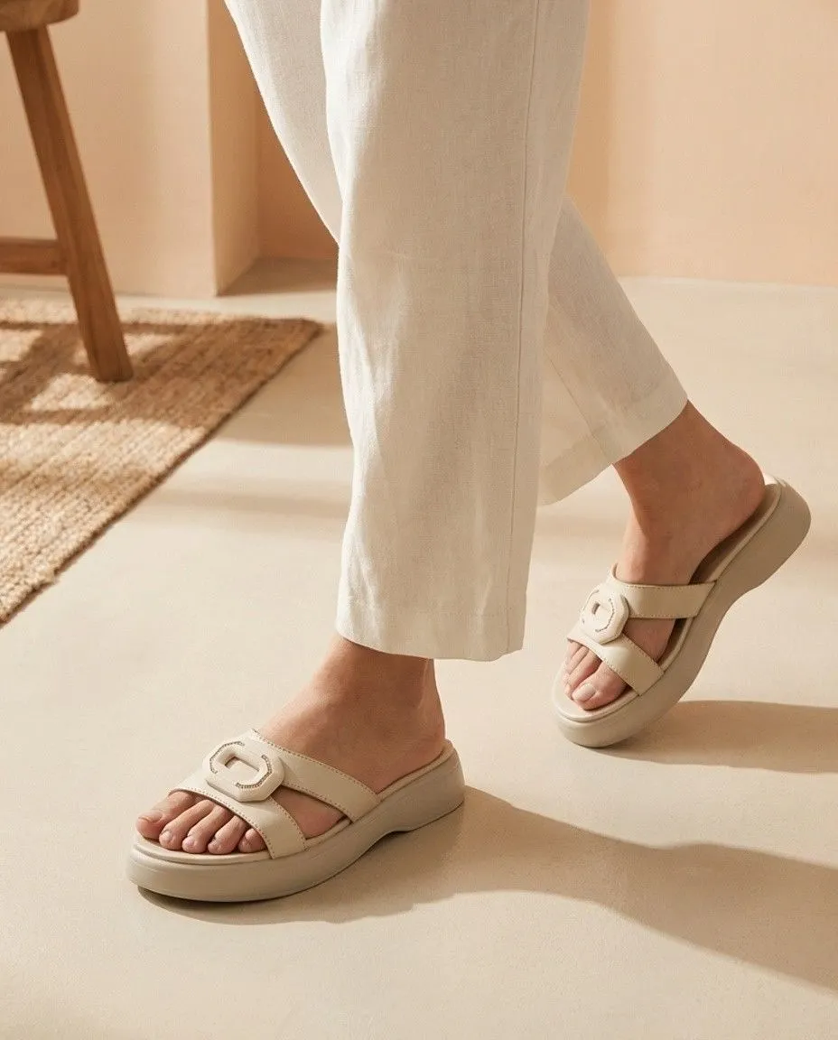 Close up of minimalist faux leather slide sandals worn with cream trousers