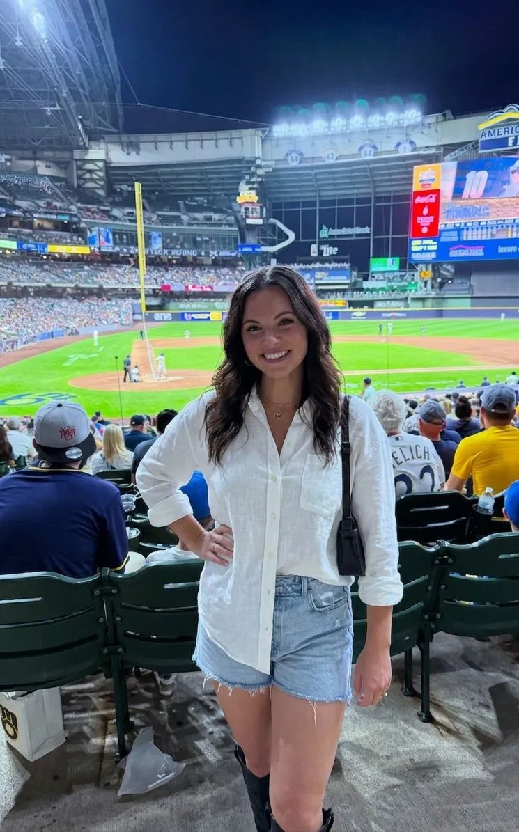 Woman wearing denim shorts and white linen shirt at a baseball game
