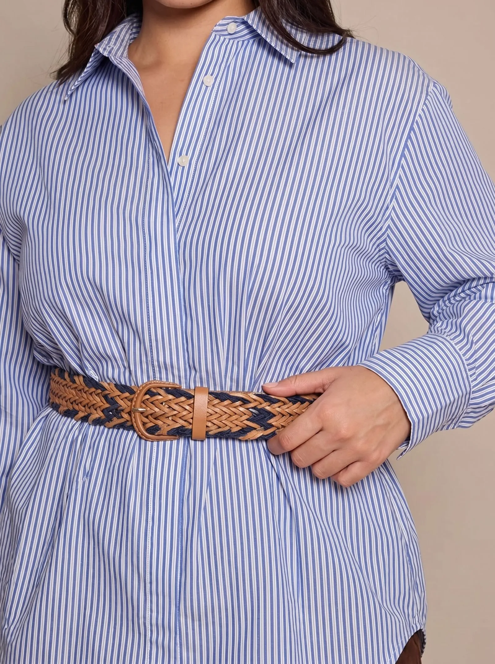 Detail shot of a woven belt cinching a blue striped poplin shirt