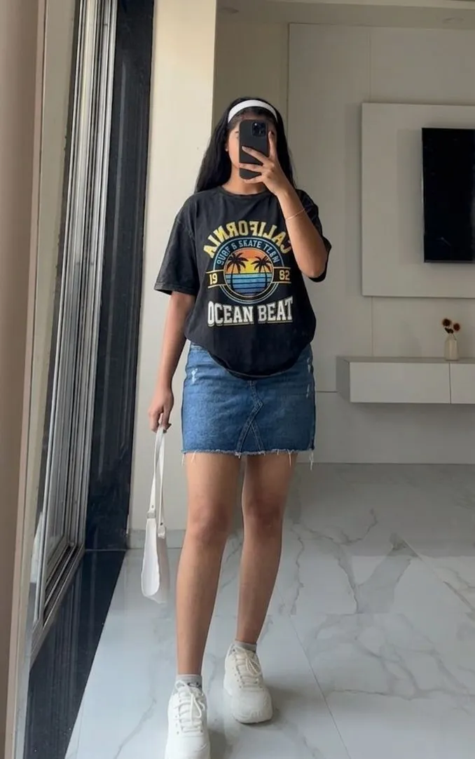 A woman posing at a baseball game in a denim mini skirt and graphic team t-shirt