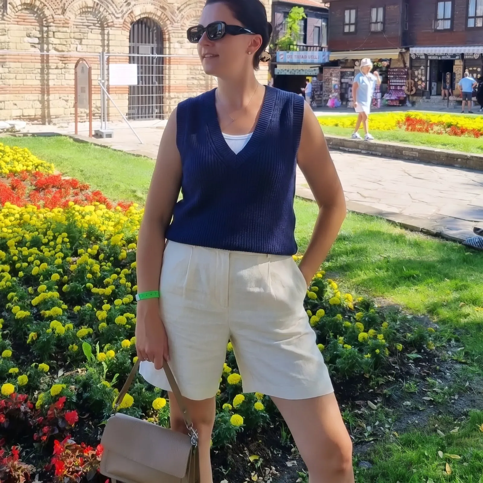 Model wearing tailored cream linen shorts and a navy blue sleeveless V-neck sweater vest