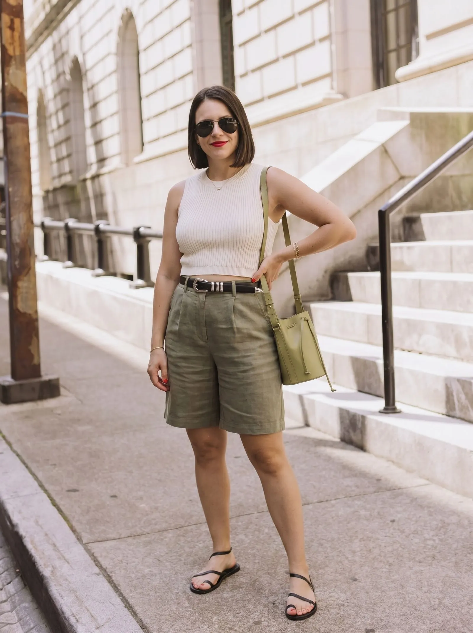 Model wearing olive green linen Bermuda shorts and ivory ribbed crop top on sunny street