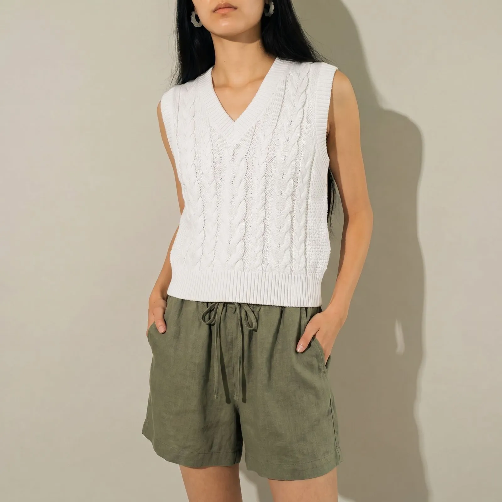 Close up of a white cotton cable-knit vest over olive green linen shorts