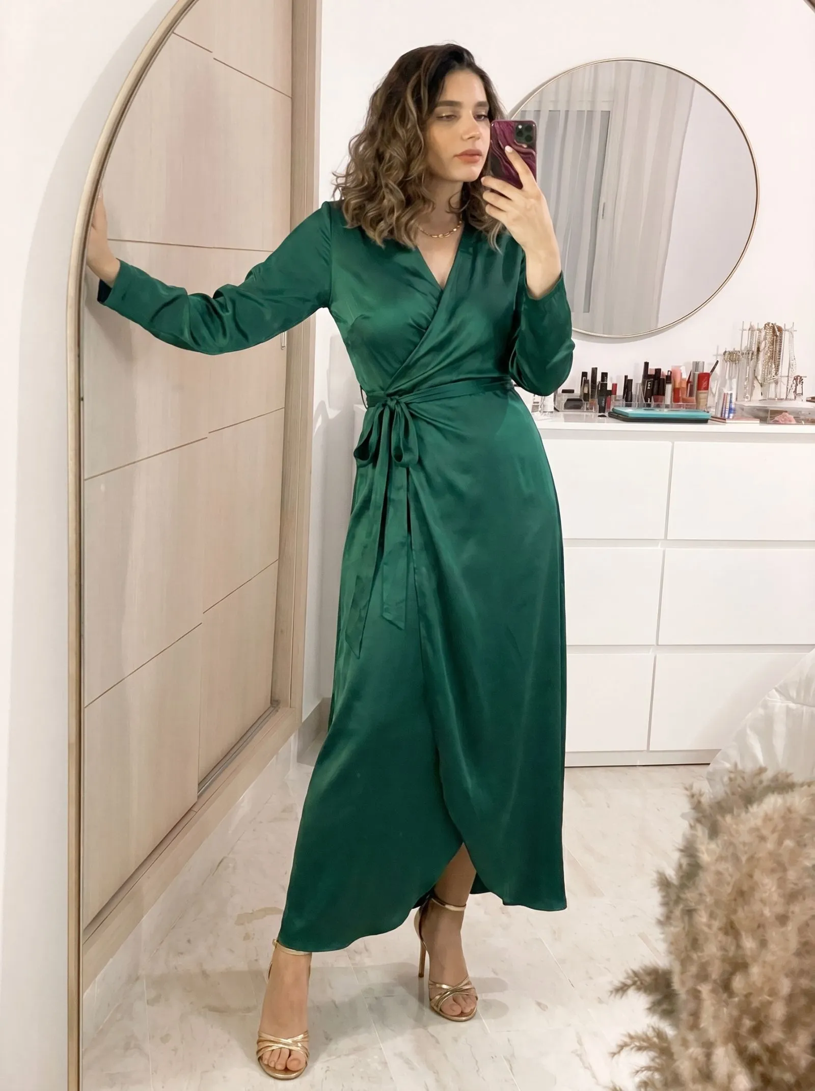 Woman wearing a sophisticated emerald green silk wrap dress and gold strappy heels for a night out