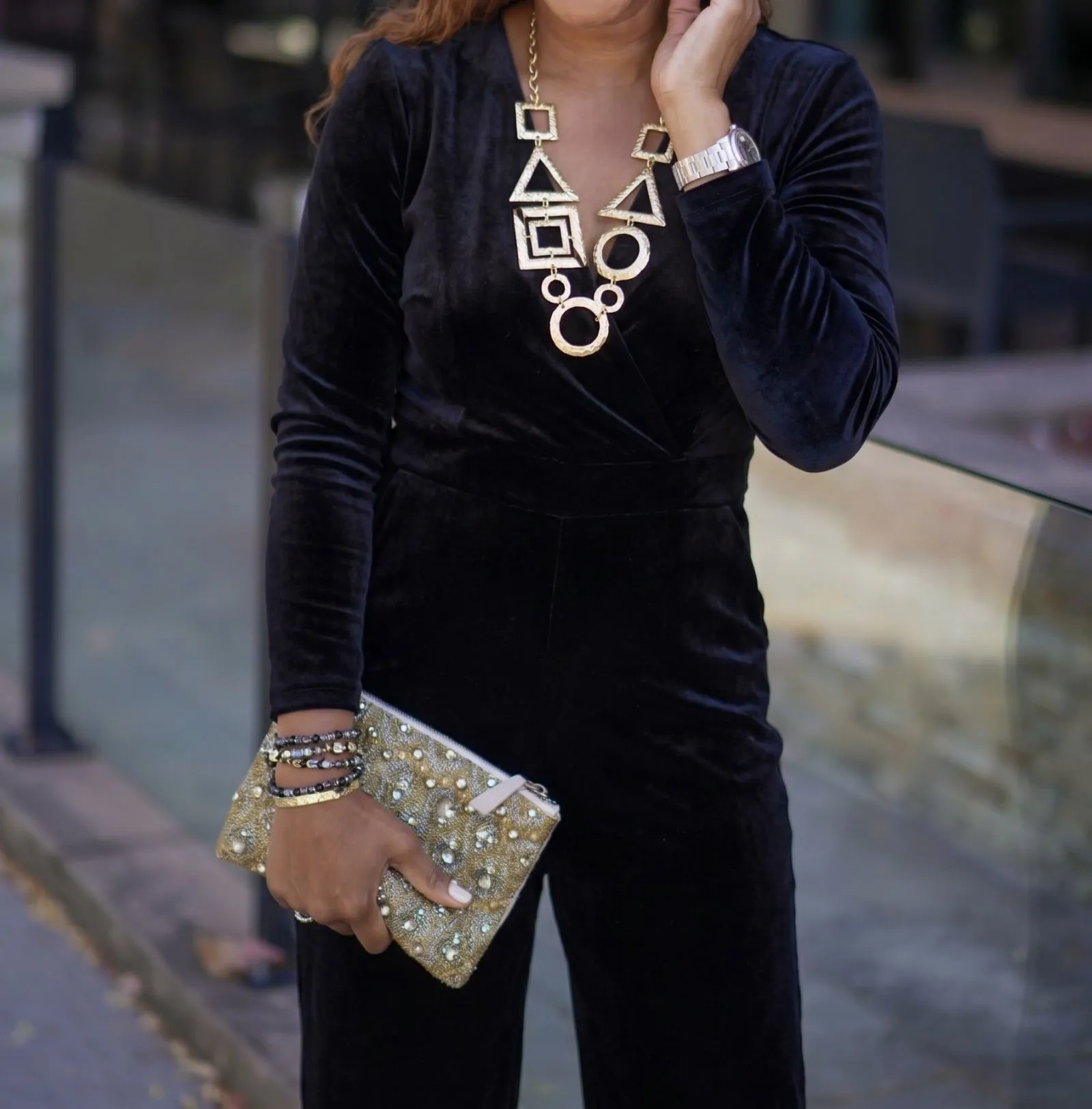 Chunky gold geometric statement necklace worn over a black velvet jumpsuit