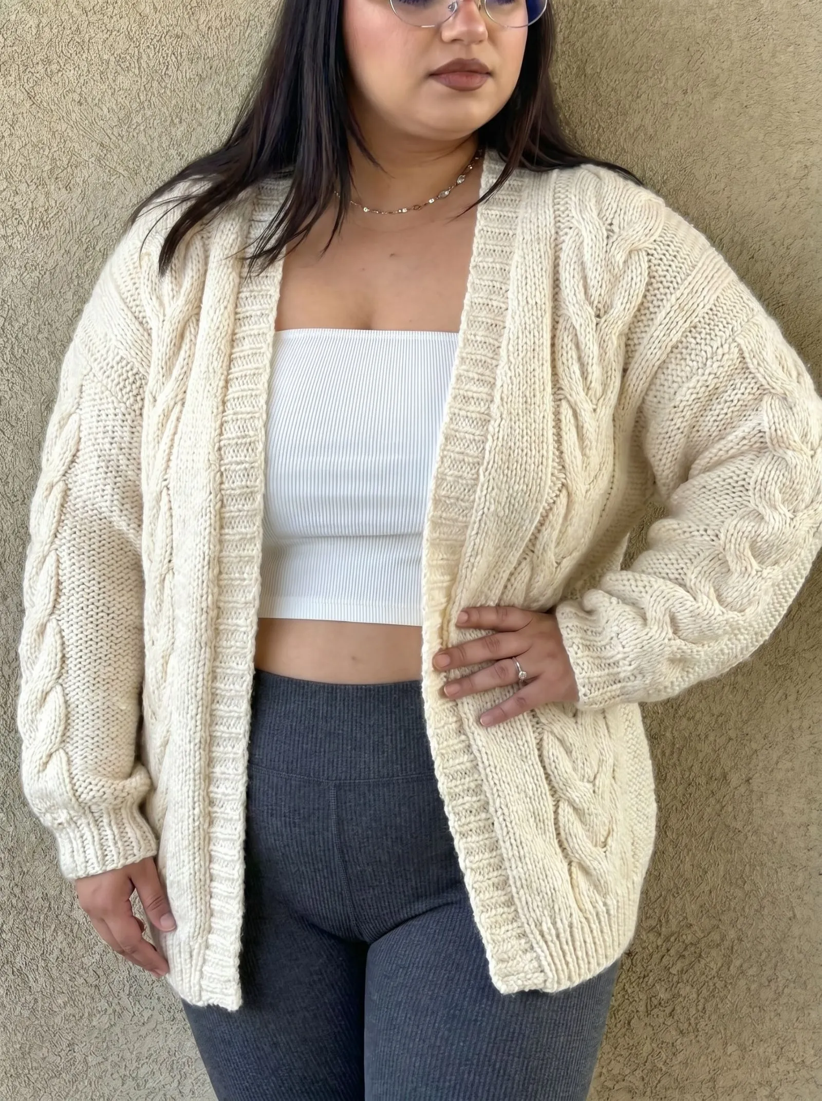 Plus size woman wearing an oversized cable knit cardigan and thermal leggings at home