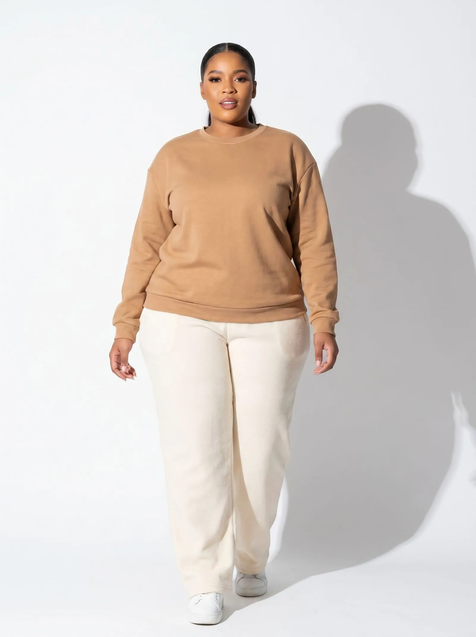 A plus size model wearing cream wide leg fleece joggers and a camel structured crewneck working from home