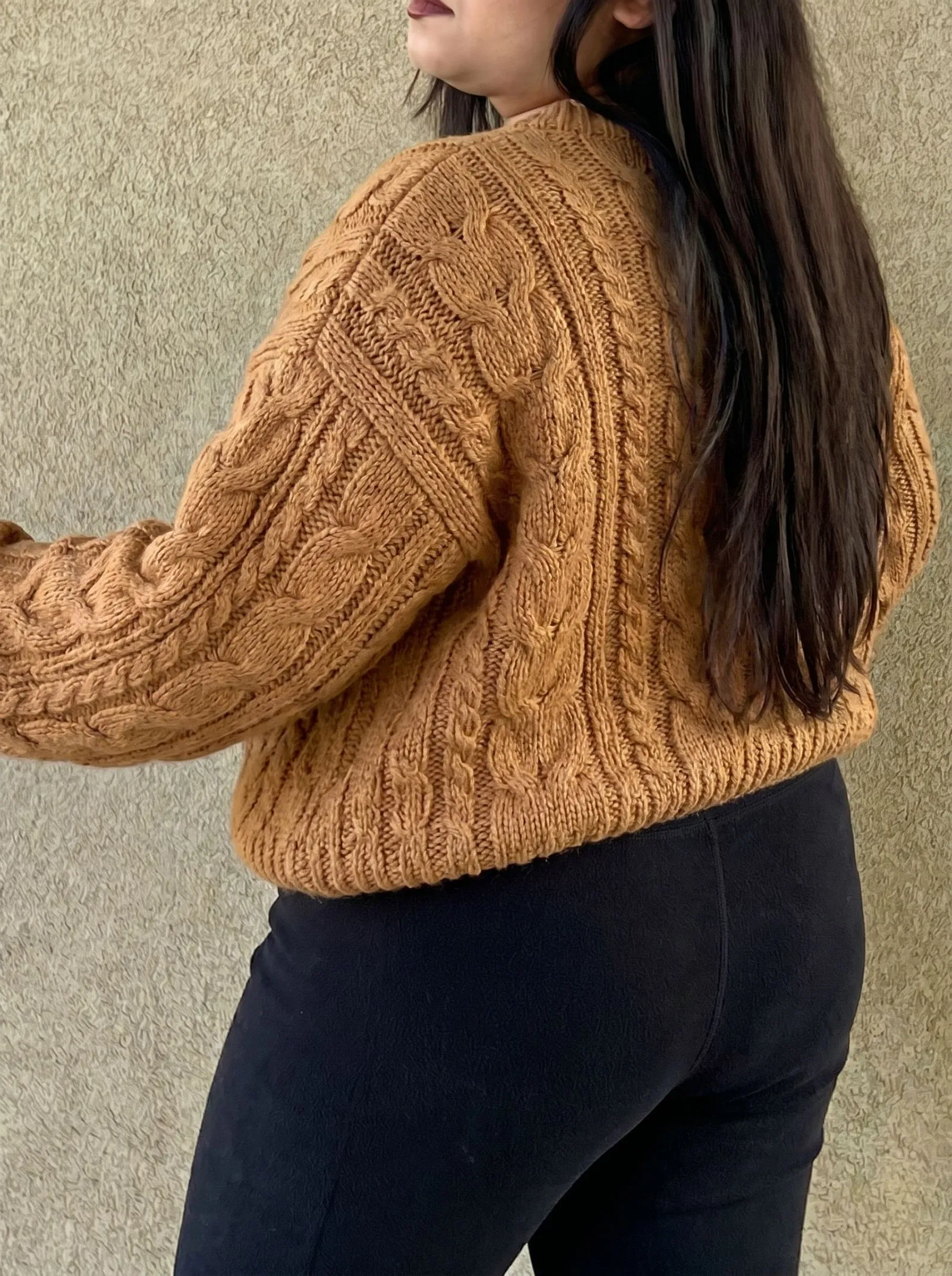 Close up of caramel cable knit sweater texture against black fleece leggings