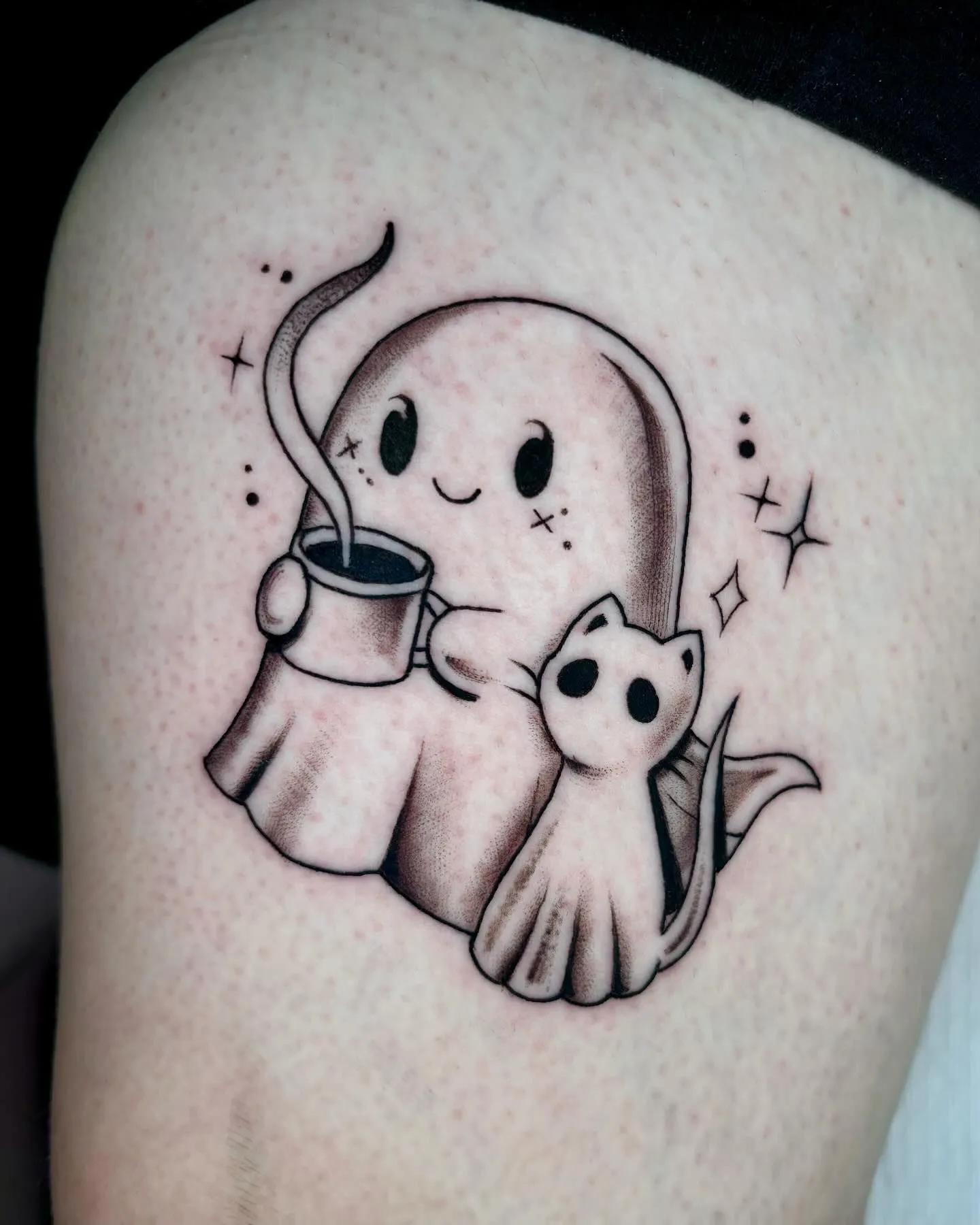 Delicate fine-line minimalist ghost holding a coffee cup tattoo on a wrist with cozy sweater sleeve